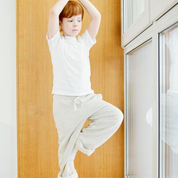 Child balancing in a tree yoga pose with intense focus.